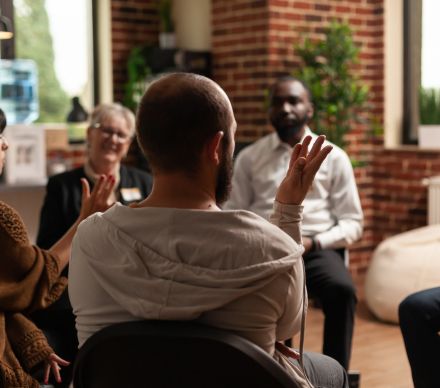 A person raising their hand to speak during a small group support meeting.