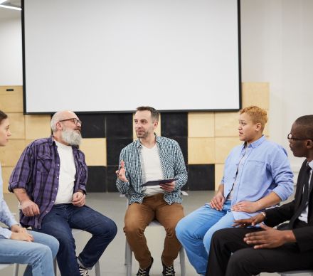 Close-up of people with clasped hands sitting in a circle during a group counseling session.
