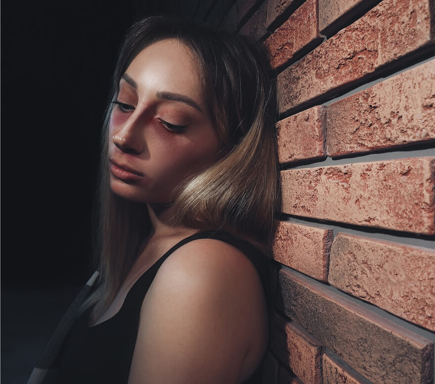 Young woman struggling with methamphetamine addiction leaning against a brick wall in a dark setting