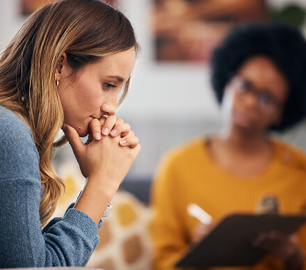 Woman sitting with clasped hands during a one-on-one therapy session with a counselor.