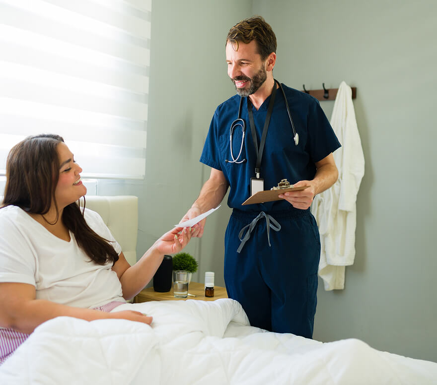 Healthcare provider in blue scrubs smiling warmly while meeting with patient on bed, supportive clinical care