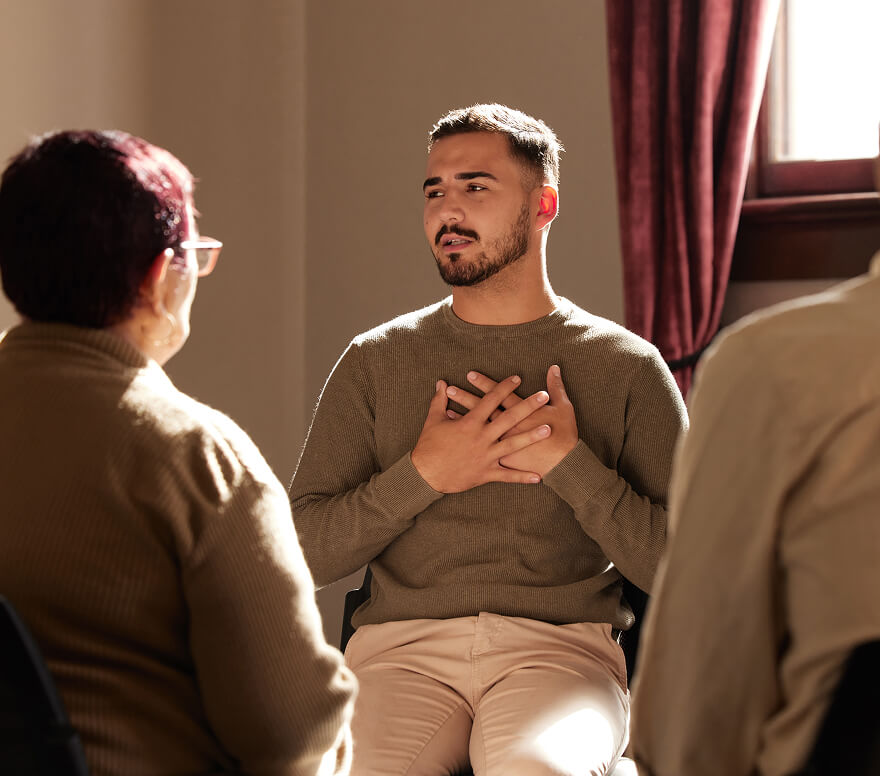 Man with hands on his chest speaking during a group therapy session