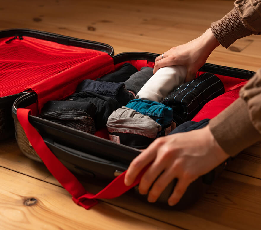 Person packing clothing and shoes into a red and black travel bag for rehab