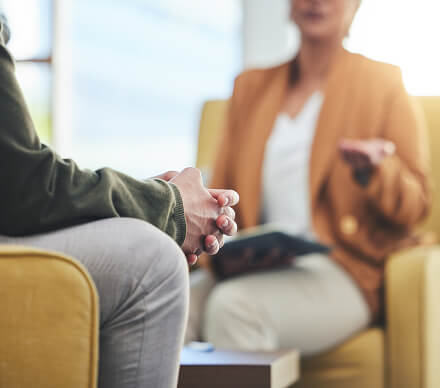 Close-up of a client's clasped hands during a counseling session, with the therapist gesturing while talking.
